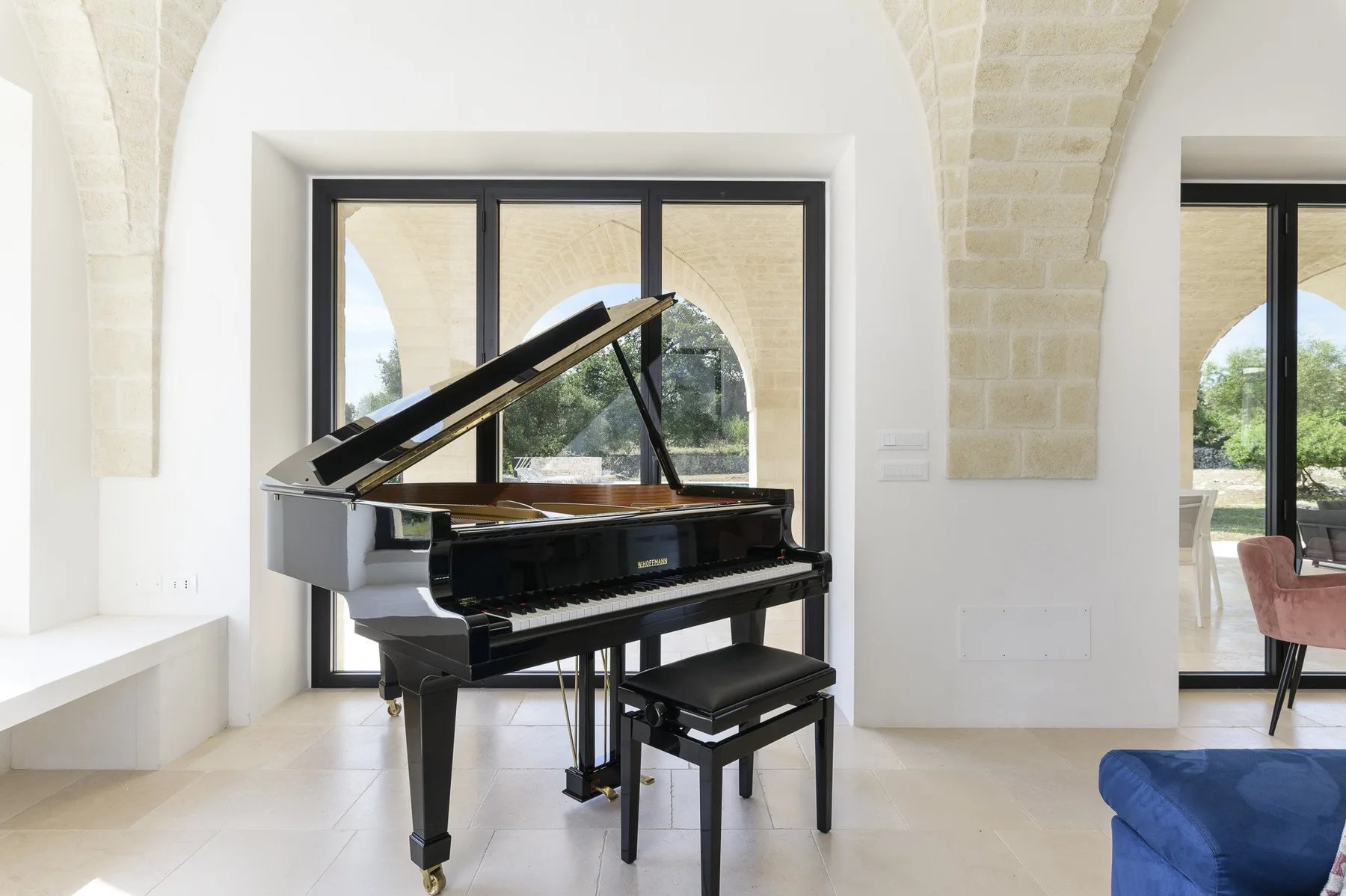 A grand piano sits in a bright room with arched stone details.