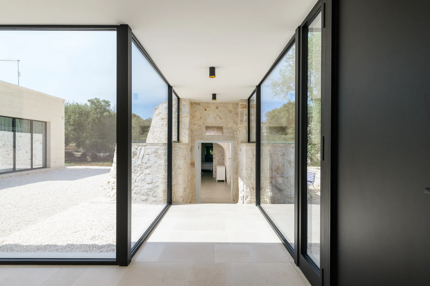 A bright glass-walled corridor leads toward a stone doorway, with an open courtyard visible outside.