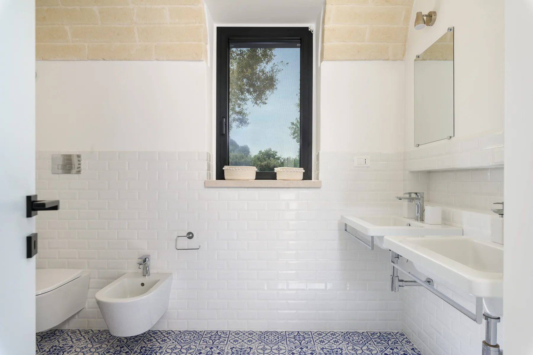 A bright tiled bathroom with a window, sink, and toilet.