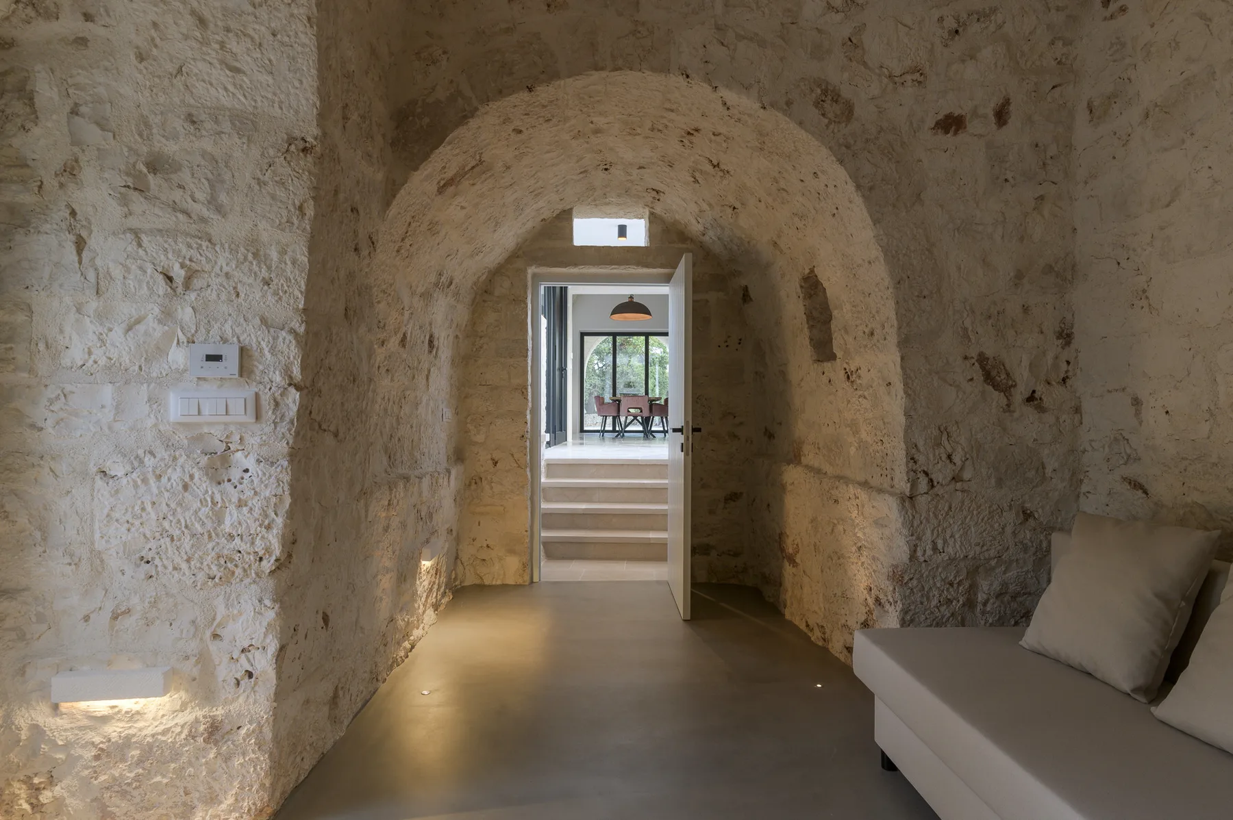 A stone interior passage opens through an arch toward a bright room.