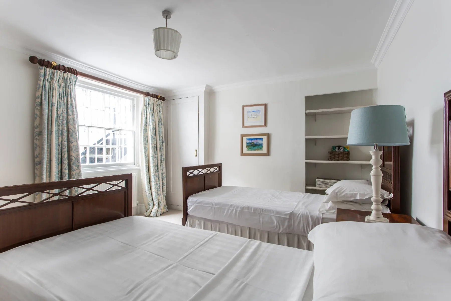 Un dormitorio con varias camas, una ventana y estanterías empotradas.