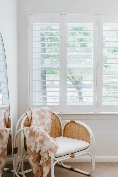 Una luminosa zona de estar con asientos tejidos junto a grandes ventanas con persianas.