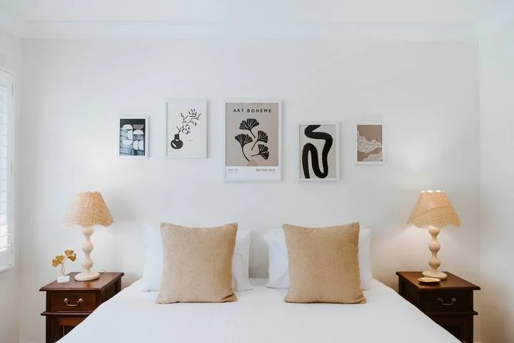 Un dormitorio luminoso tiene una cama bien tendida bajo cuadros en la pared.