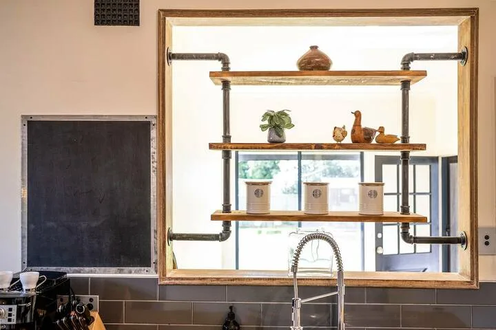 Una encimera de cocina con estantes abiertos y un grifo frente a una ventana.