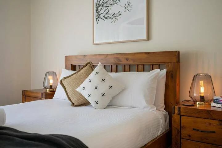 Un dormitorio con una cama de madera, ropa de cama blanca y lámparas de noche.