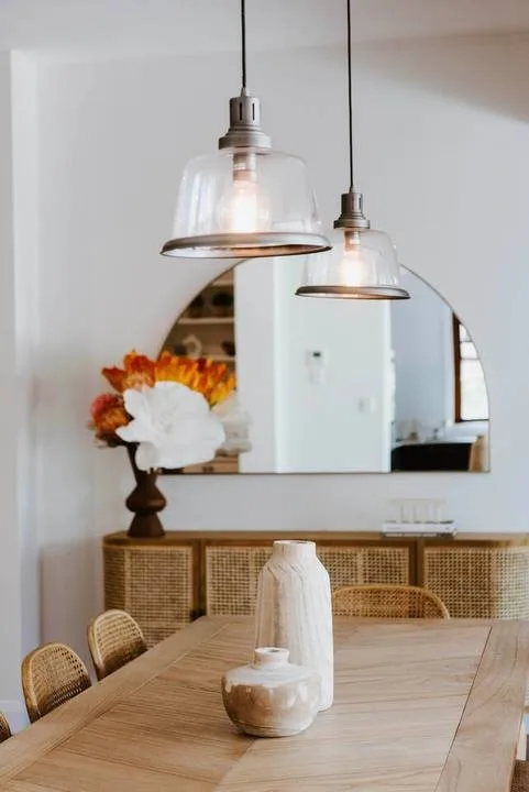 Un comedor con una mesa de madera, lámparas colgantes y un espejo de pared.
