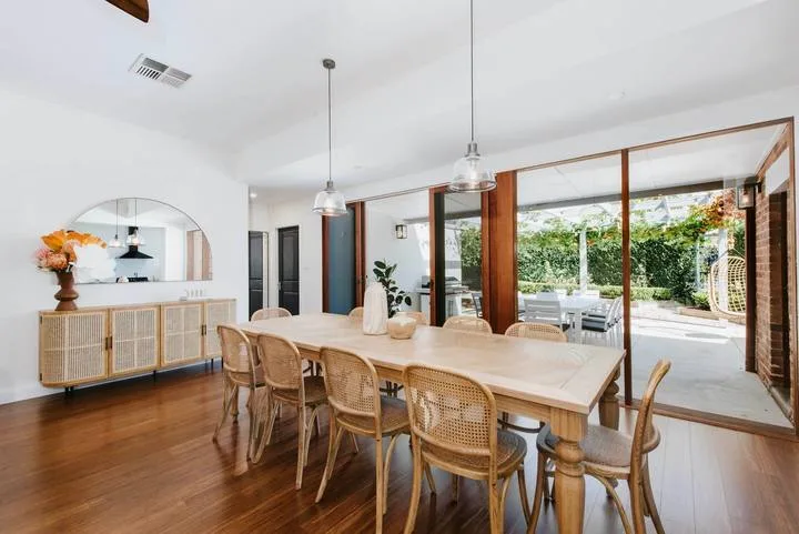 Un comedor luminoso con una larga mesa de madera junto a puertas de vidrio abiertas al patio.