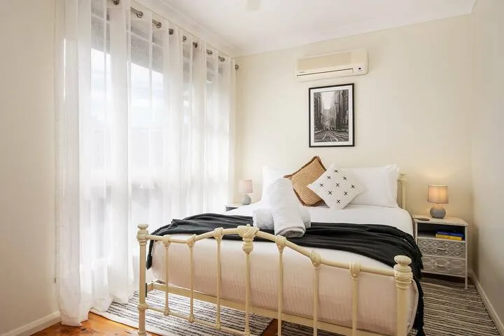 Un dormitorio luminoso con una cama, cortinas translúcidas y una mesita de noche.