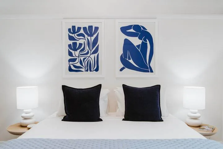Un dormitorio luminoso con una cama tendida y arte azul sobre ella.