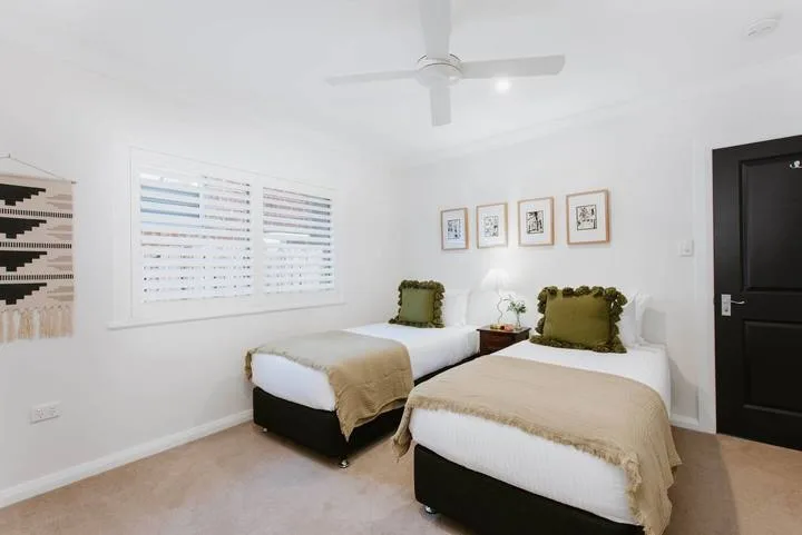 Un dormitorio luminoso con dos camas, almohadas verdes y un ventilador de techo.