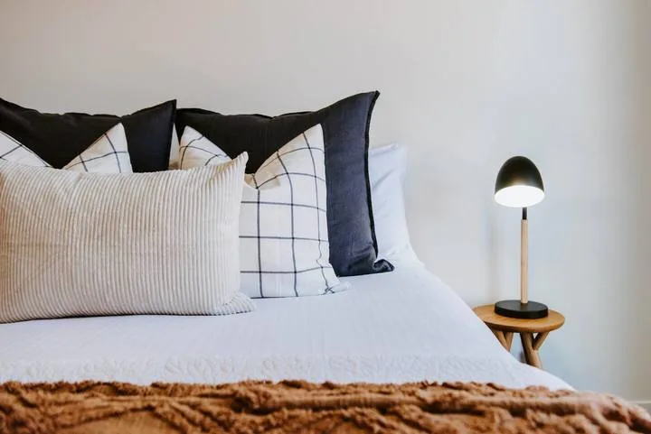 Una cama bien arreglada con almohadas estampadas y una lámpara de noche.