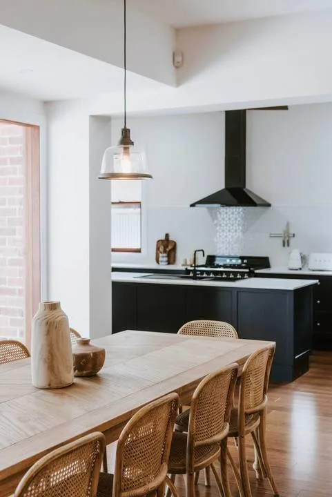 Comedor con mesa de madera y asientos tejidos junto a una cocina moderna.