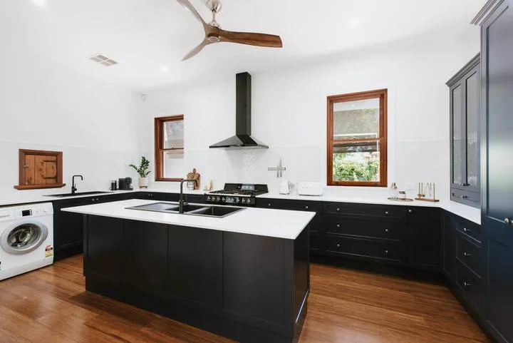 Una cocina luminosa con gabinetes oscuros, una isla central y piso de madera.