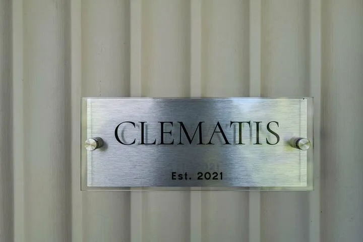 Un letrero metálico que dice «Clematis» está montado en una pared acanalada verticalmente.
