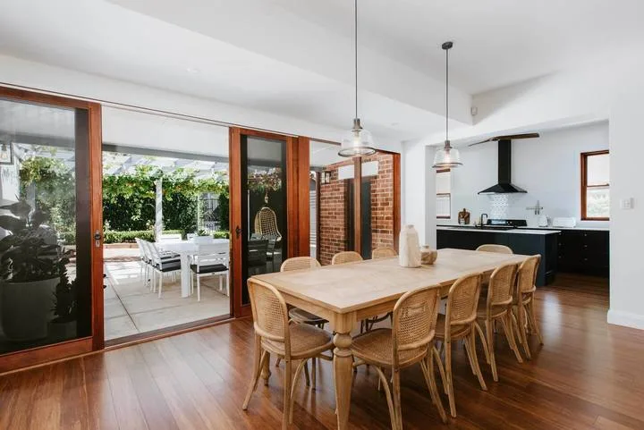 A dining area with a long wooden table beside an open kitchen and patio.