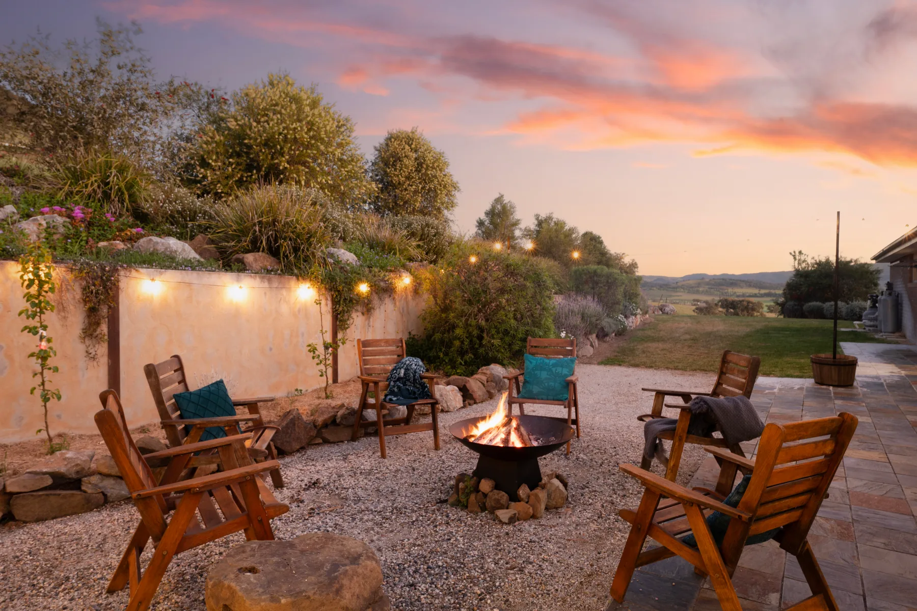 An outdoor seating area surrounds a fire pit beneath a colorful sunset sky.