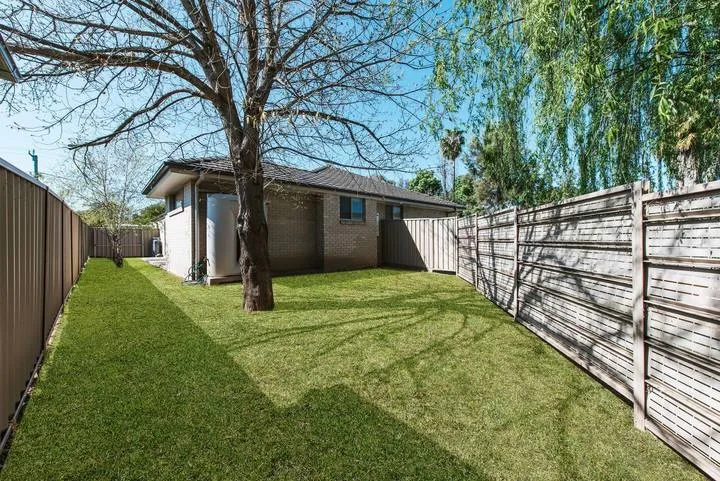 Un patio cercado con césped, un árbol y un edificio pequeño.