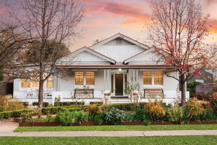 Una casa blanca se alza detrás de un jardín bajo un cielo de atardecer colorido.