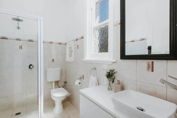 Un baño luminoso con ducha de vidrio, inodoro y lavabo.
