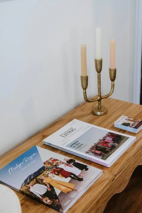 Una mesa de madera muestra revistas junto a un portavelas de latón.
