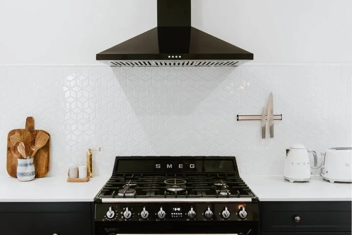 Una zona de cocina con una estufa debajo de una campana oscura.