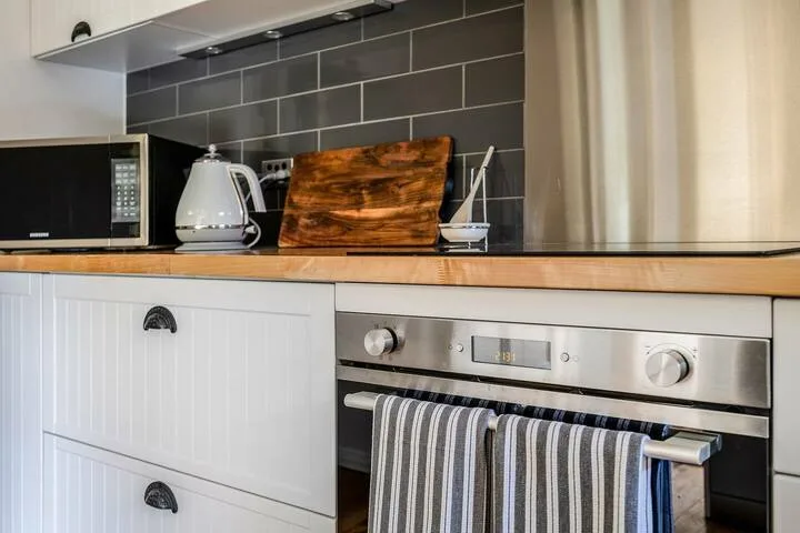 Una encimera de cocina con una tetera y una tabla de cortar sobre un horno.