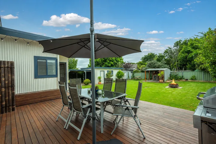 Una zona de comedor al aire libre está en una terraza de madera junto a un césped verde.
