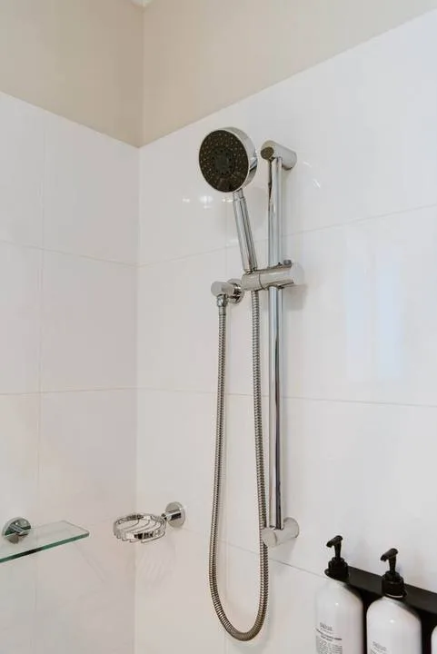Una zona de ducha con azulejos, ducha de mano y controles montados en la pared.