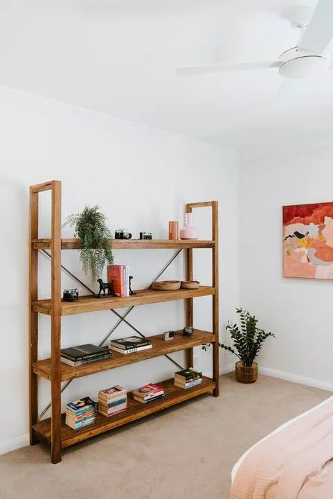 Una habitación luminosa tiene una estantería de madera con libros y plantas.