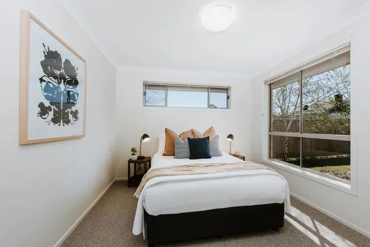 Un dormitorio luminoso con una cama bien tendida bajo una ventana estrecha.