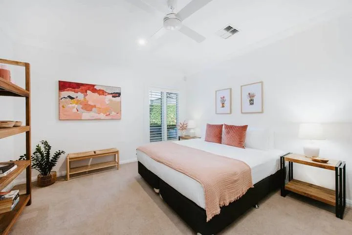 Un dormitorio luminoso con una cama tendida y cuadros en las paredes.