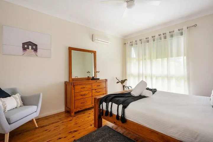 Un dormitorio luminoso con una cama de madera, una cómoda y cortinas translúcidas.
