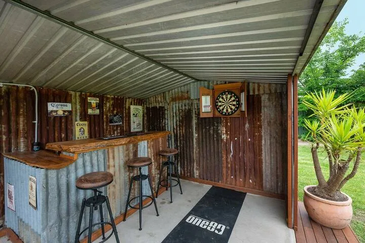 Una zona de bar al aire libre cubierta tiene una barra, taburetes y una diana.