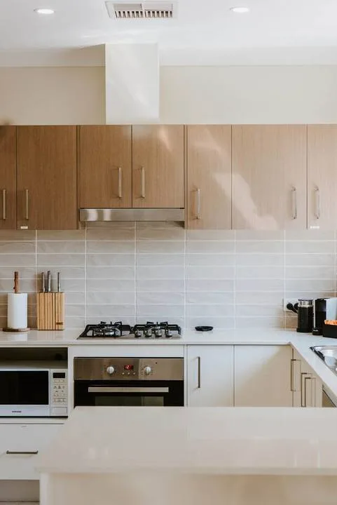 Una cocina moderna con gabinetes de madera, un salpicadero de azulejos y electrodomésticos integrados.