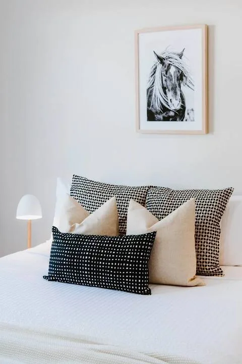 Una cama bien arreglada con cojines estampados y un dibujo enmarcado de un caballo encima.