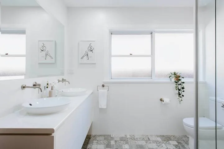 Un baño luminoso con lavabo doble, ventanas amplias y una ducha de vidrio.