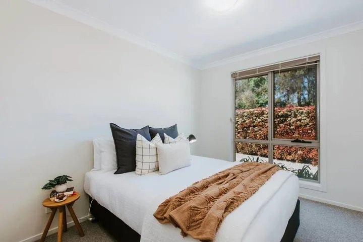 Un dormitorio luminoso con una cama vestida de blanco y una ventana amplia.