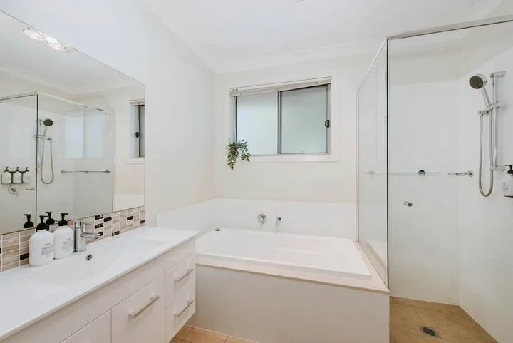 Un baño luminoso con bañera, ducha de vidrio y un tocador largo.