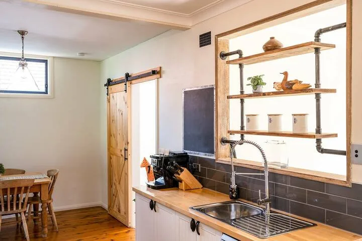 Una encimera de cocina con fregadero y estantes abiertos de madera junto a un comedor.