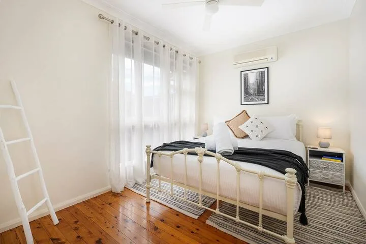 Un dormitorio luminoso con una cama, cortinas translúcidas y suelo de madera.