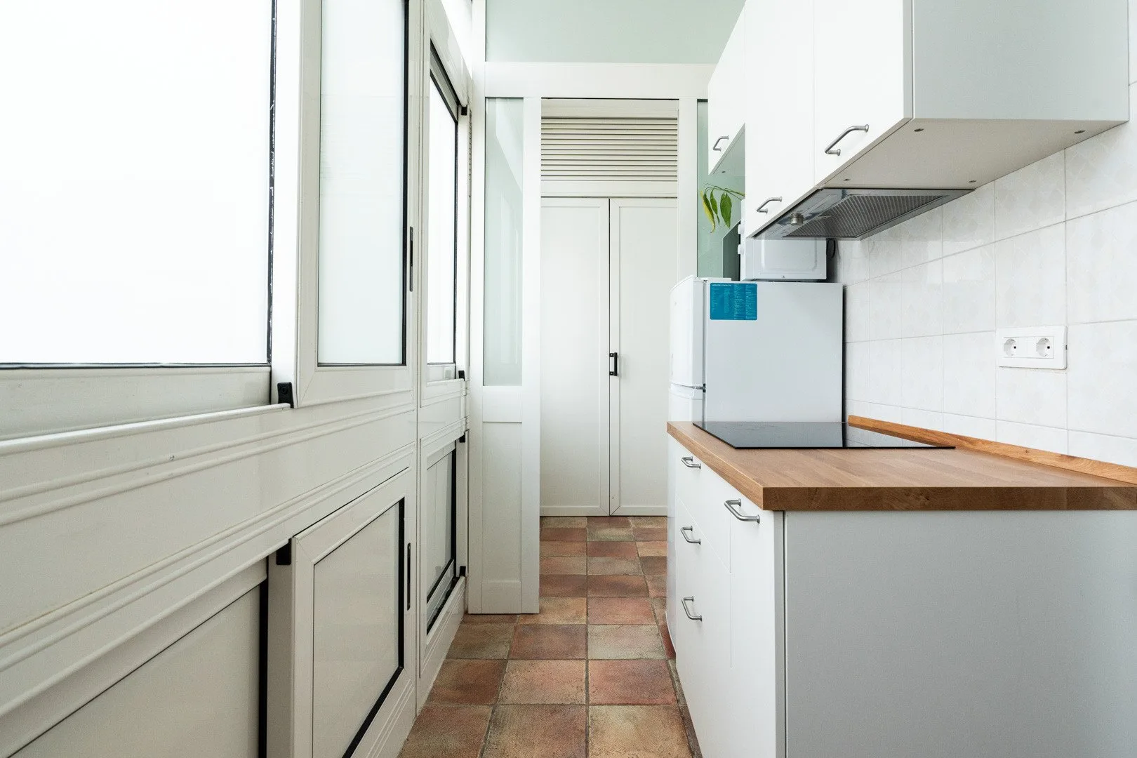A narrow kitchen with white cabinets, a wooden countertop, and large windows.
