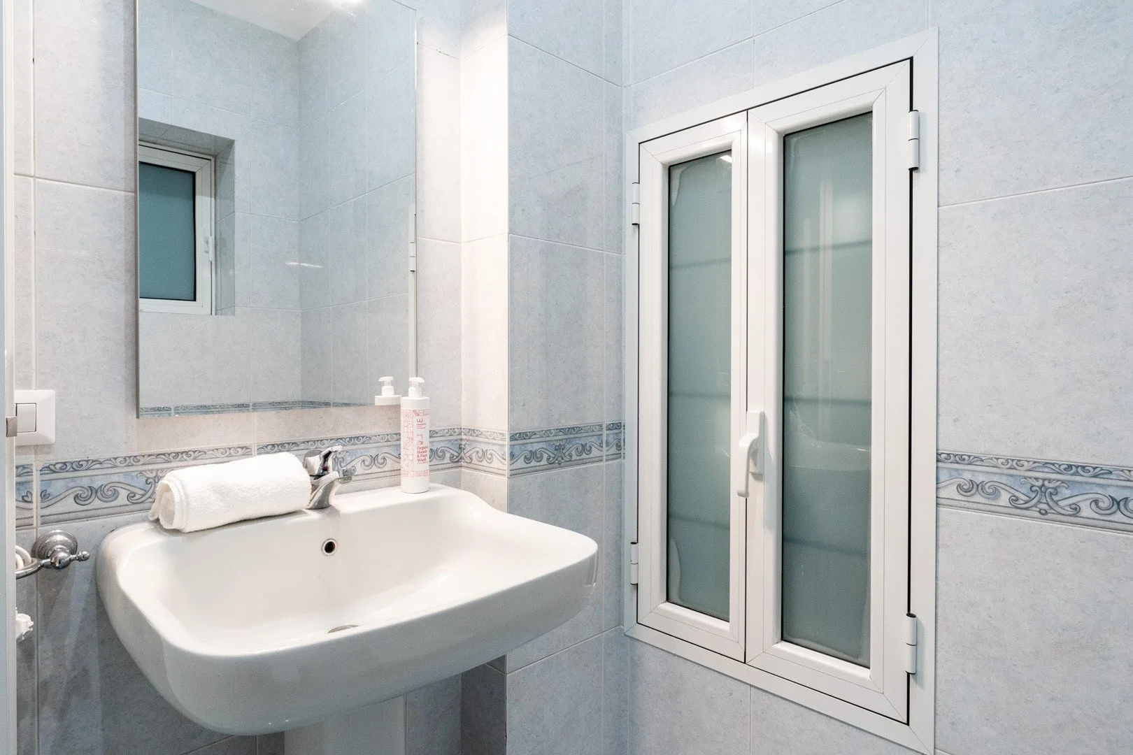 A tiled bathroom with a white sink and a frosted-glass window.