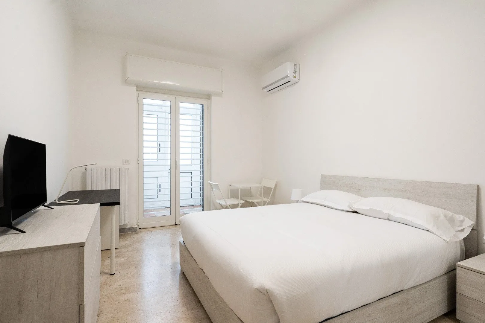 Un dormitorio luminoso con una cama grande, un televisor y puertas de vidrio.