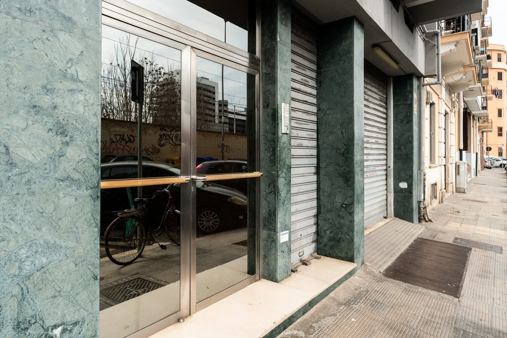 A glass storefront entrance opens onto a paved sidewalk along a city street.
