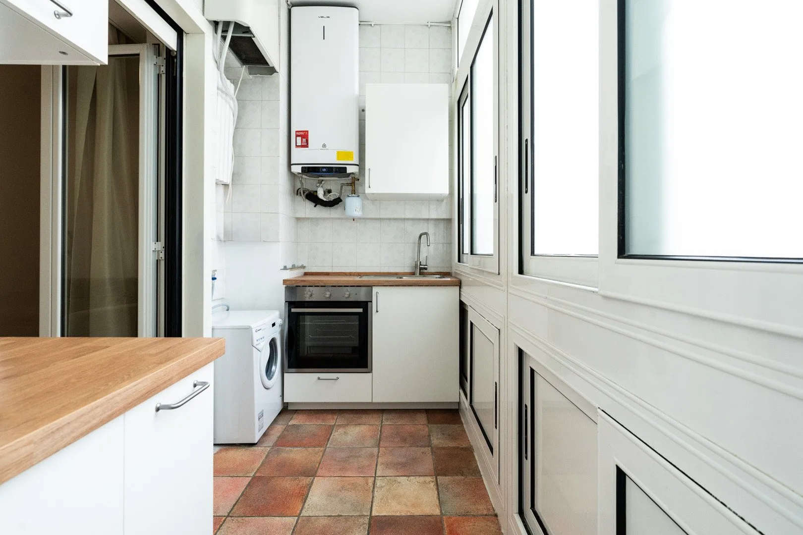 A compact kitchen with a countertop, built-in oven, and large windows.