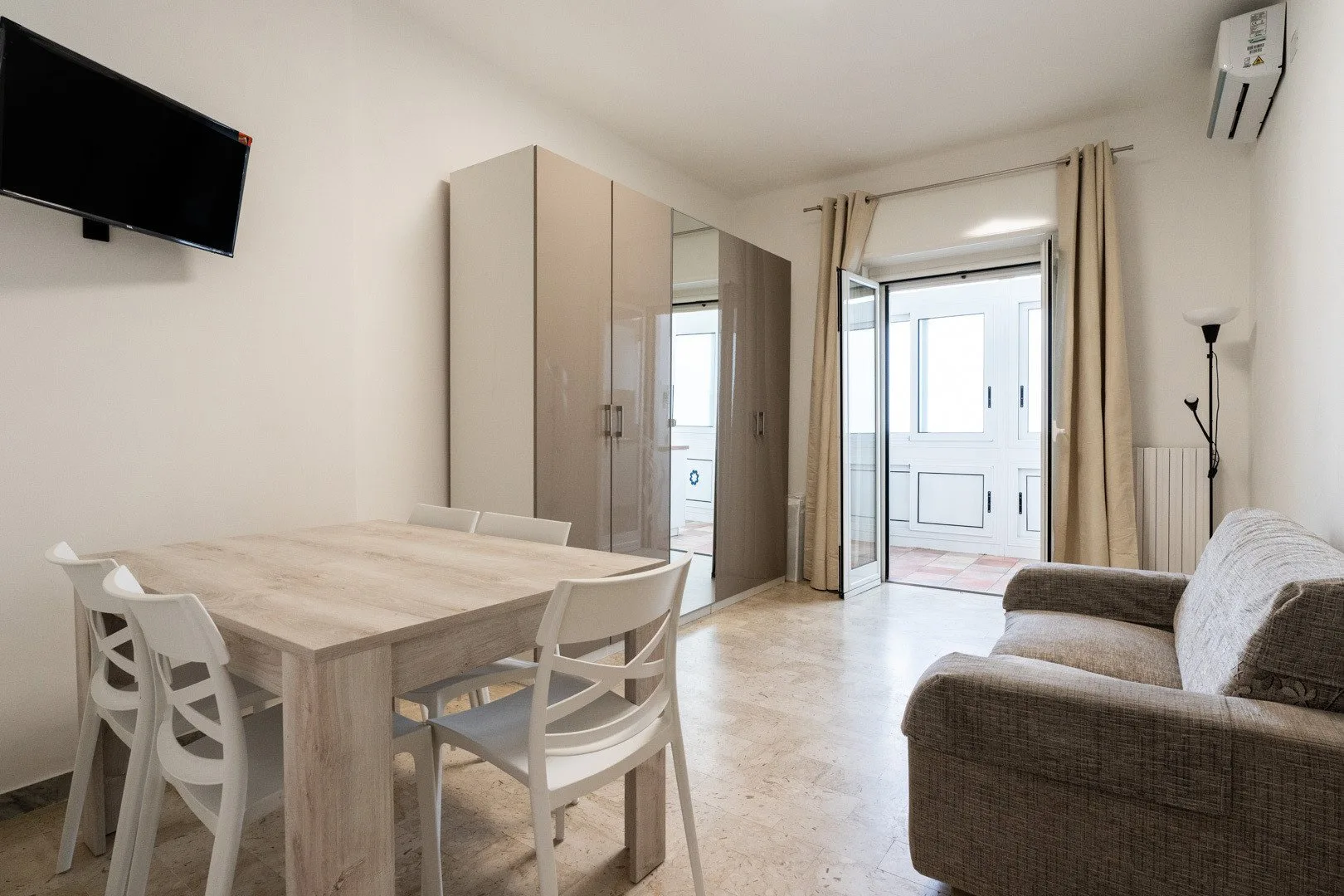A bright living and dining area with a table, seating, and a large window.
