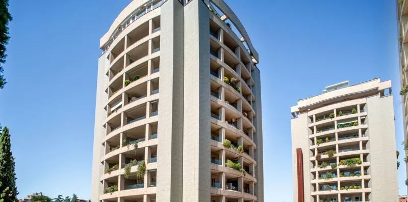 High-rise residential buildings with stacked balconies stand beneath a clear blue sky.