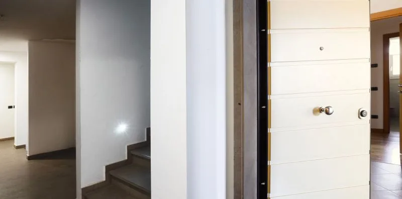 An interior hallway with a staircase beside an open entrance door.