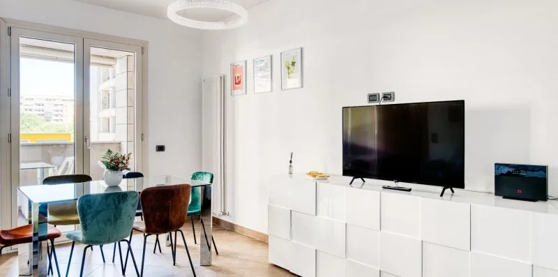 A dining area and television are shown beside tall glass doors opening onto a balcony.