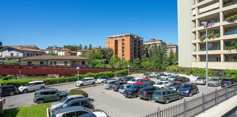 A parking lot filled with cars sits beside several apartment buildings.